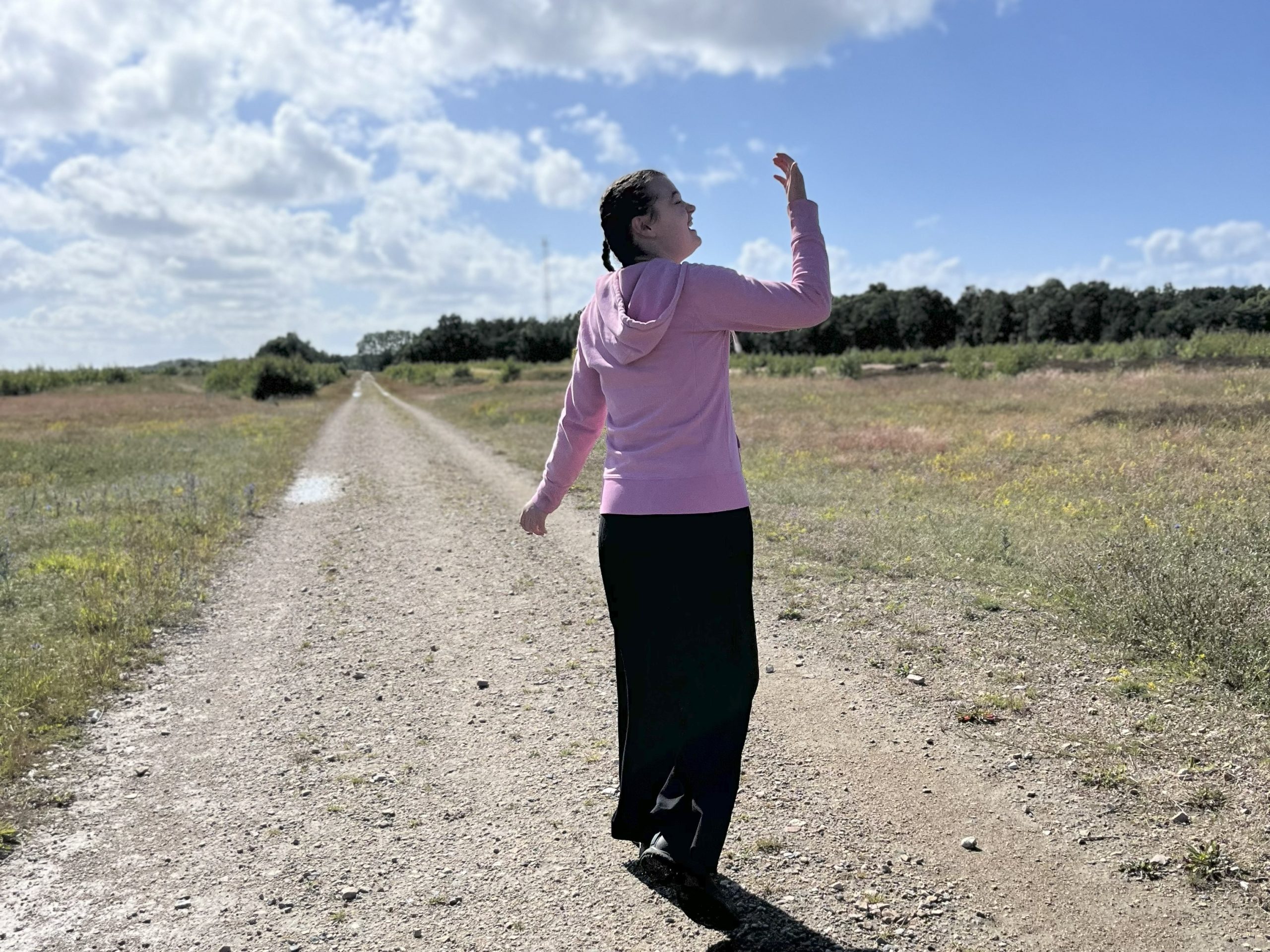 Flicka gående på grusväg som ler och håller upp handen mot himlen och känner lycka och välmående.