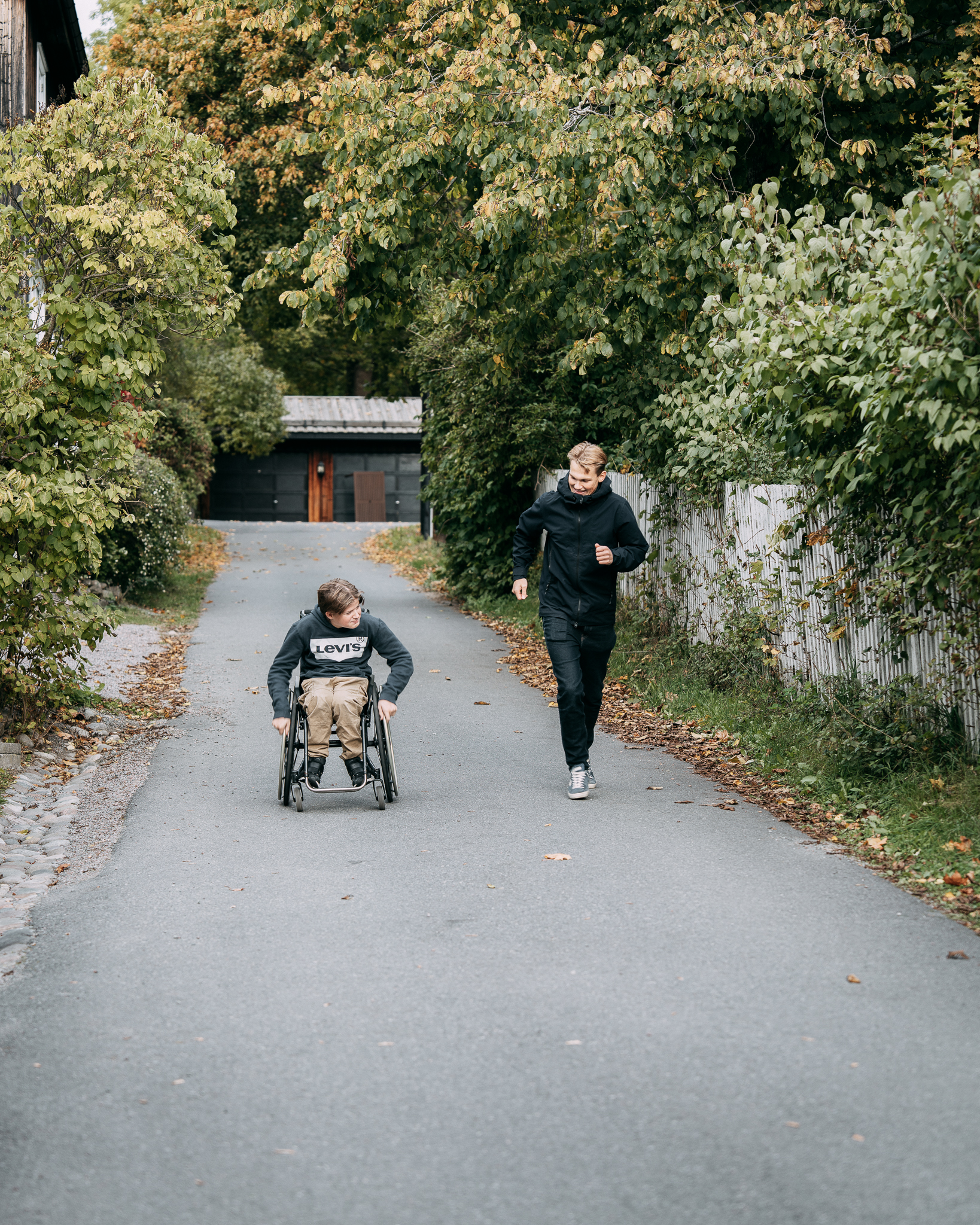 Pojke i rullstol på en väg och manlig personlig assistent springandes bredvid.